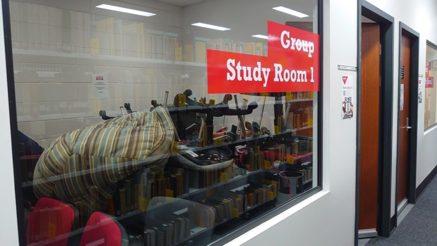 A window looking into a room labelled ‘Group Study Room 1’, which is packed full of chairs.
