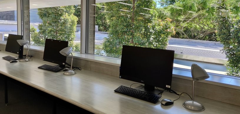 Computers on a long desk in front of a window.