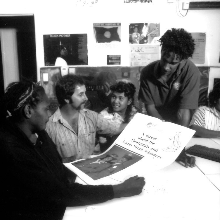 Four people sitting around a desk looking at a poster.