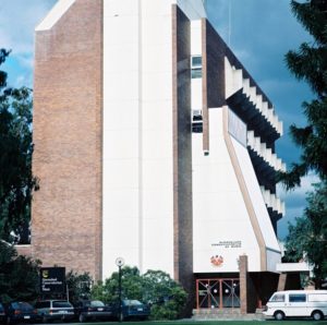 Former Conservatorium building at Gardens Point QUT Campus. Cars are parked in front of the building and a cloudy blue sky makes up the background.