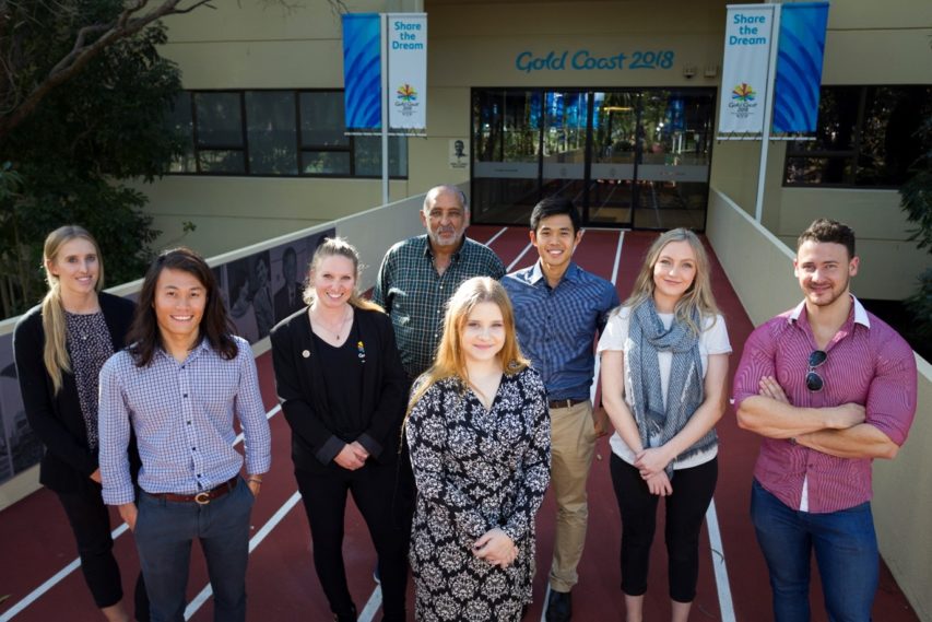 Eight interns stand in front of a building with Gold Coast 2018 written above the doors.