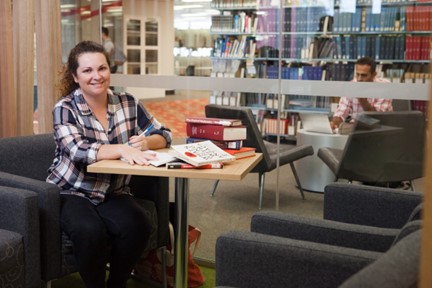 A person sitting at a table in the library. There are books on the table.