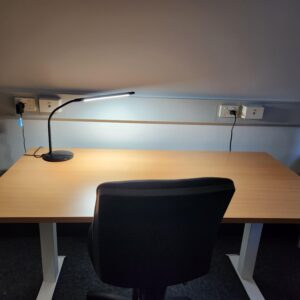 A desk with a desk lamp and chair in a room with low lighting.