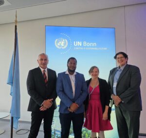 Johanna stands with three other people in front of a sign that reads “UN Bonn: Shaping a sustainable future”.