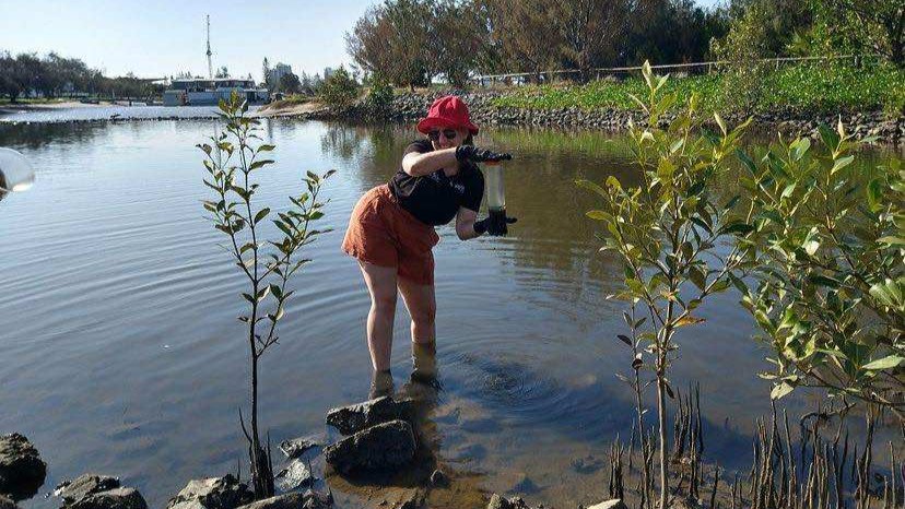 Mackenzie standing in ankle-deep water and holding a water sample container.